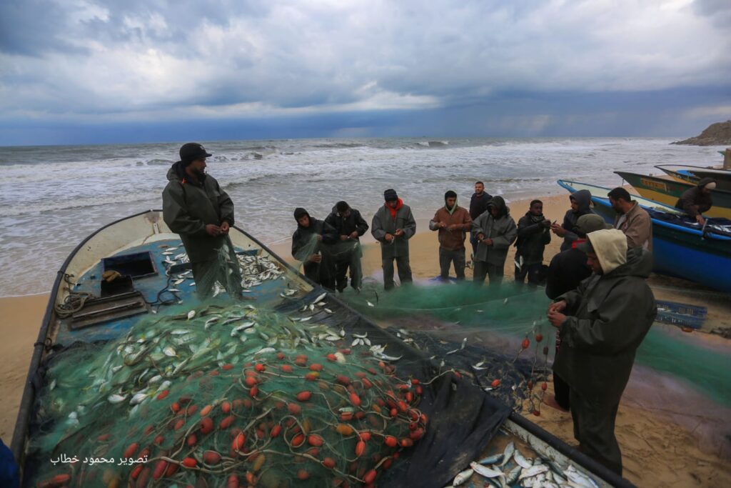 صيادون فلسطينيون يزيلون الأسماك التي اصطادوها من شبكة الصيد على شاطىء بحر دير البلح في قطاع غزة بعد ثلاثة أيام من اغلاقه (بعدسة محمود خطاب)
