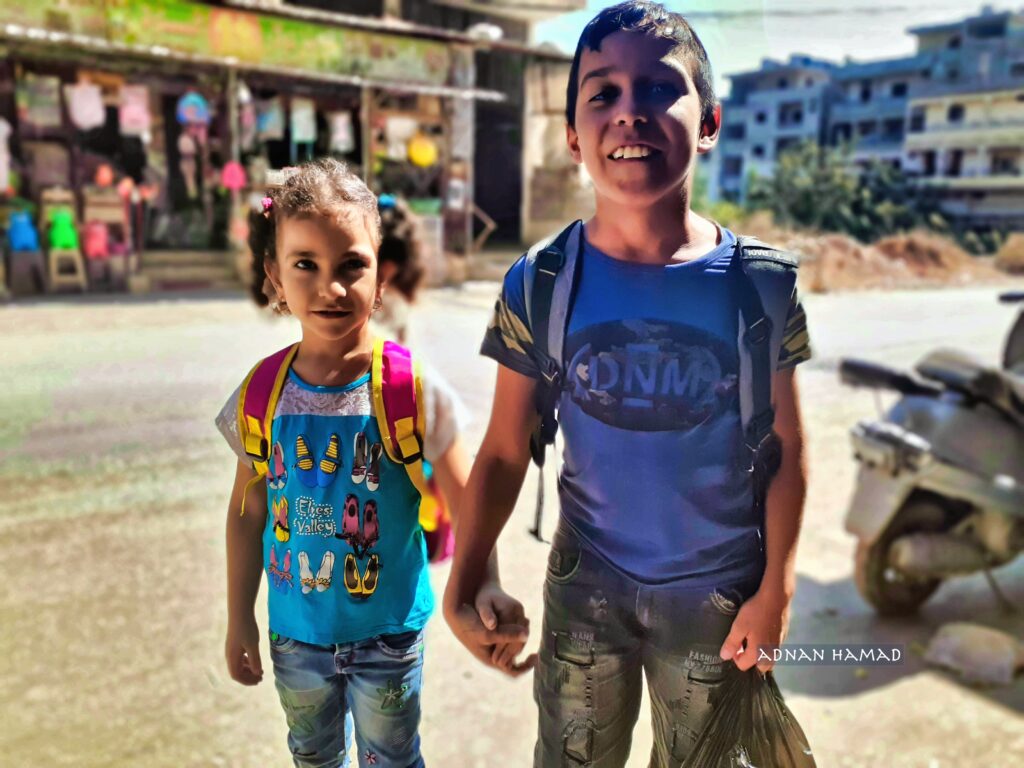 طفل يمسك بيد شقيقته أثناء عودتهما من المدرسة في مخيم نهر البارد للاجئين الفلسطينيين، طرابلس، شمال لبنان (بعدسة عدنان الحمد)
