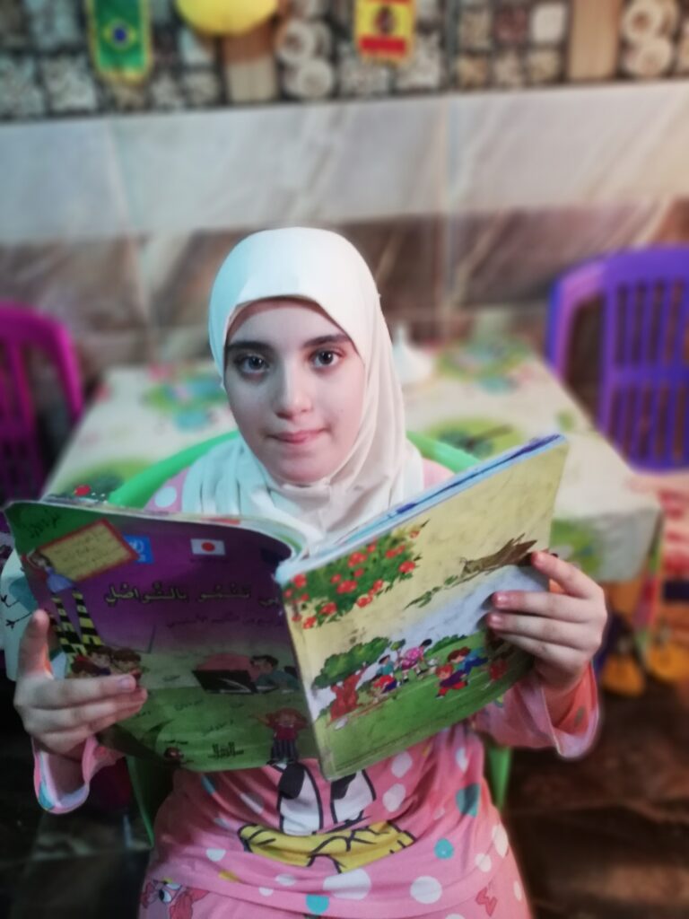 الطفلة إيمان خليل من مخيم عين الحلوة للاجئين الفلسطينيين تقرأ درساً في كتاب اللغة العربية (بعدسة رشا حيدر)