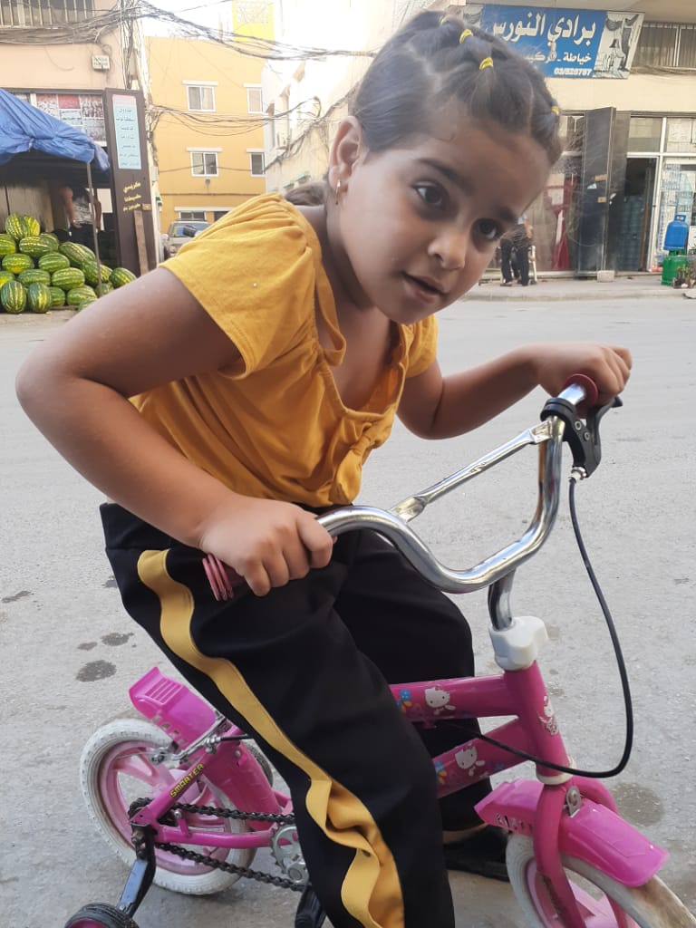 طفلة تلهو على دراجتها في أحد شوارع مخيم نهر البارد للاجئين الفلسطينيين في مدينة طرابلس، شمال لبنان (بعدسة عدنان الحمد)