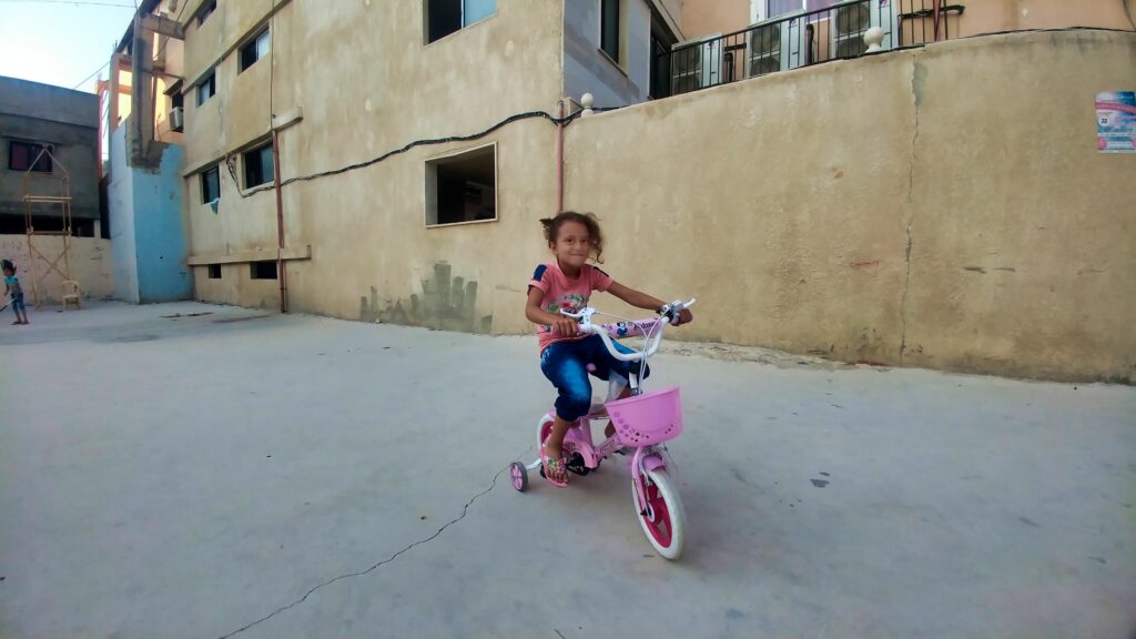 طفلة على دراجتها في حي الكورنيش في مخيم نهر البارد للاجئين الفلسطينيين في مدينة طرابلس، شمال لبنان (بعدسة عدنان الحمد)