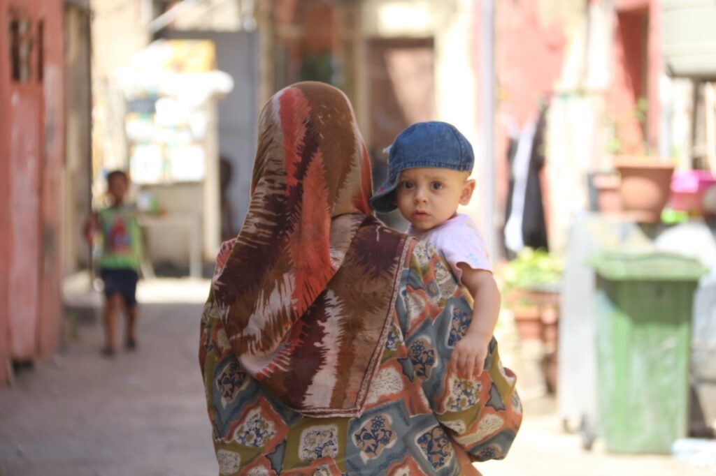 أم تحمل طفلها في مخيم البص في صور، جنوب لبنان، (بعدسة رانية سعد الله).