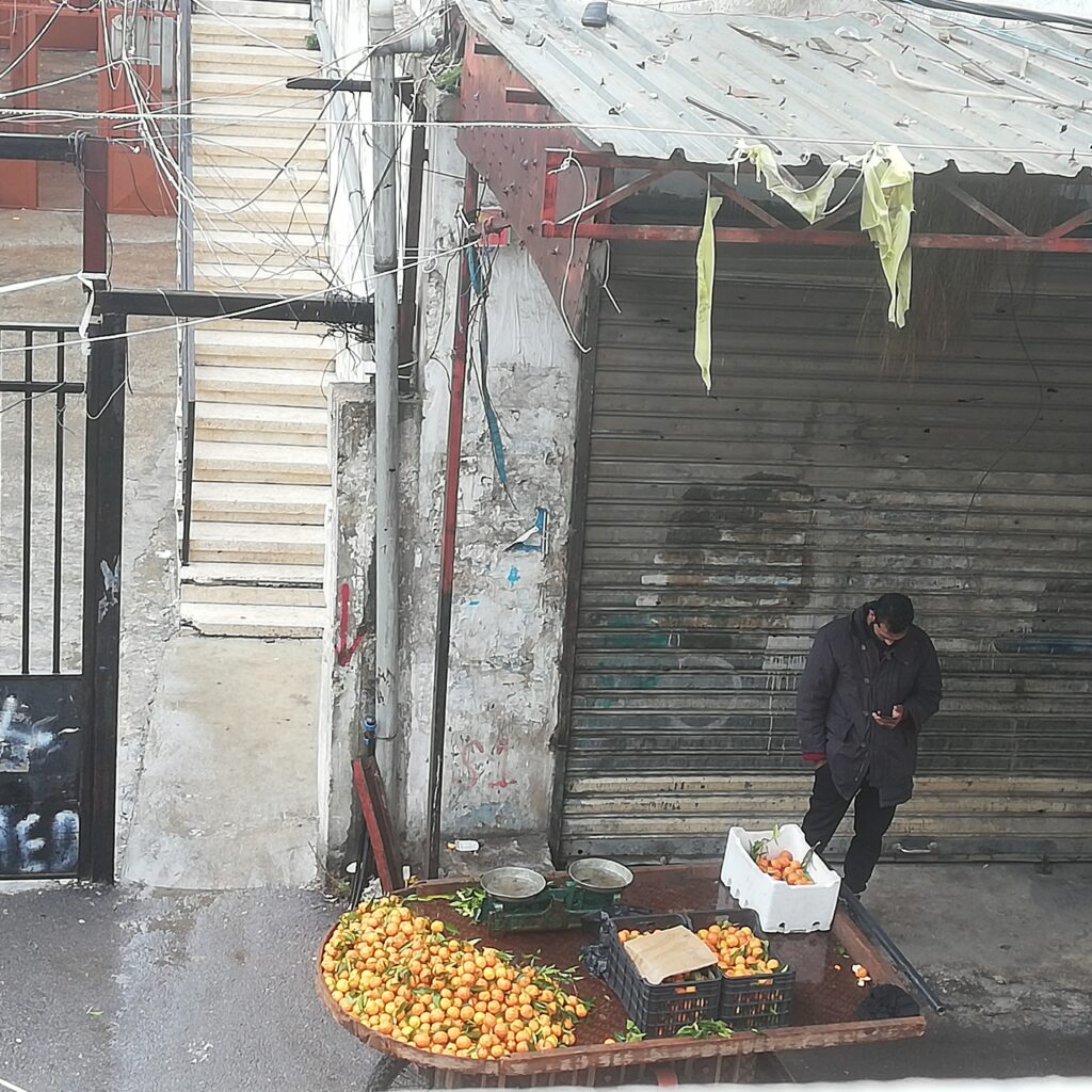 بائع البرتقال سليمان يقضي وقته على هاتفه الجوال في إنتظار الزبائن في الشارع الفوقاني في مخيم عين الحلوة للاجئين الفلسطينيين، صيدا، جنوب لبنان (بعدسة رشا حيدر)